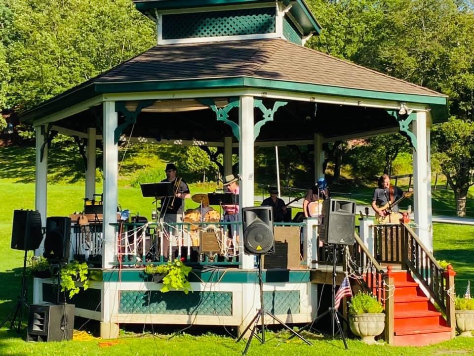 A band setting up and playing at the Wood Park gazebo in the late afternoon sun.