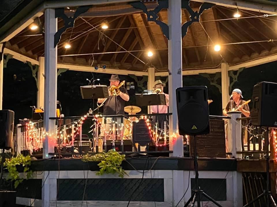Trumpet, trombone, and guitar on stage at the Wood Park gazebo after dark.