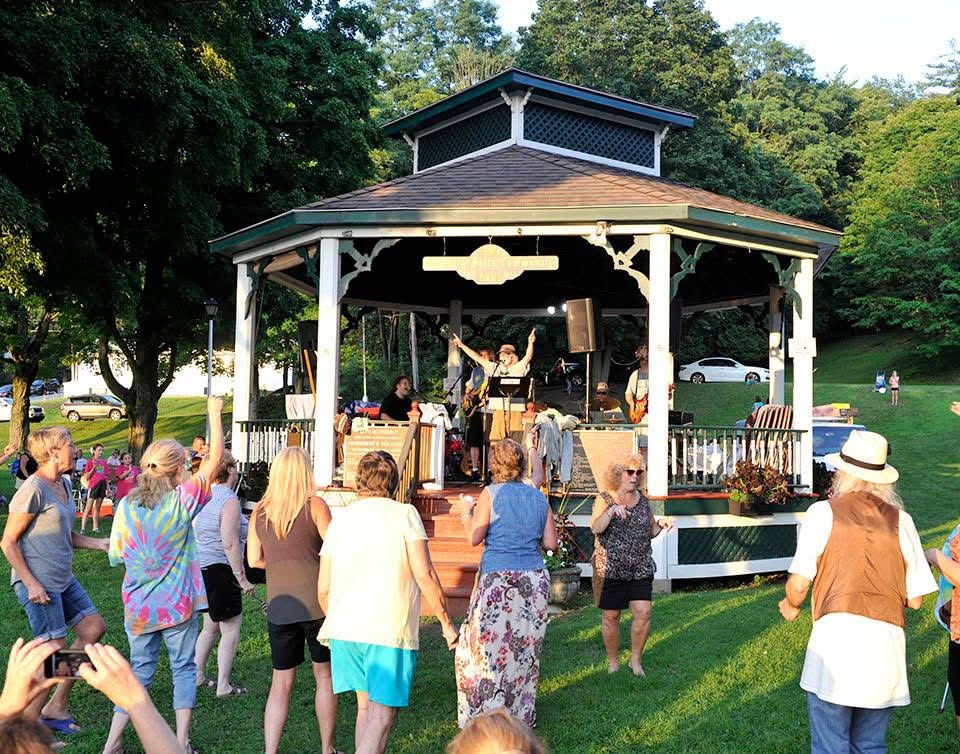 Neighbors gathered with hands raised in front of the gazebo on a summer evening.