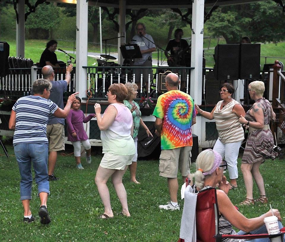 A group dancing on the grass in front of the gazebo while the band plays.