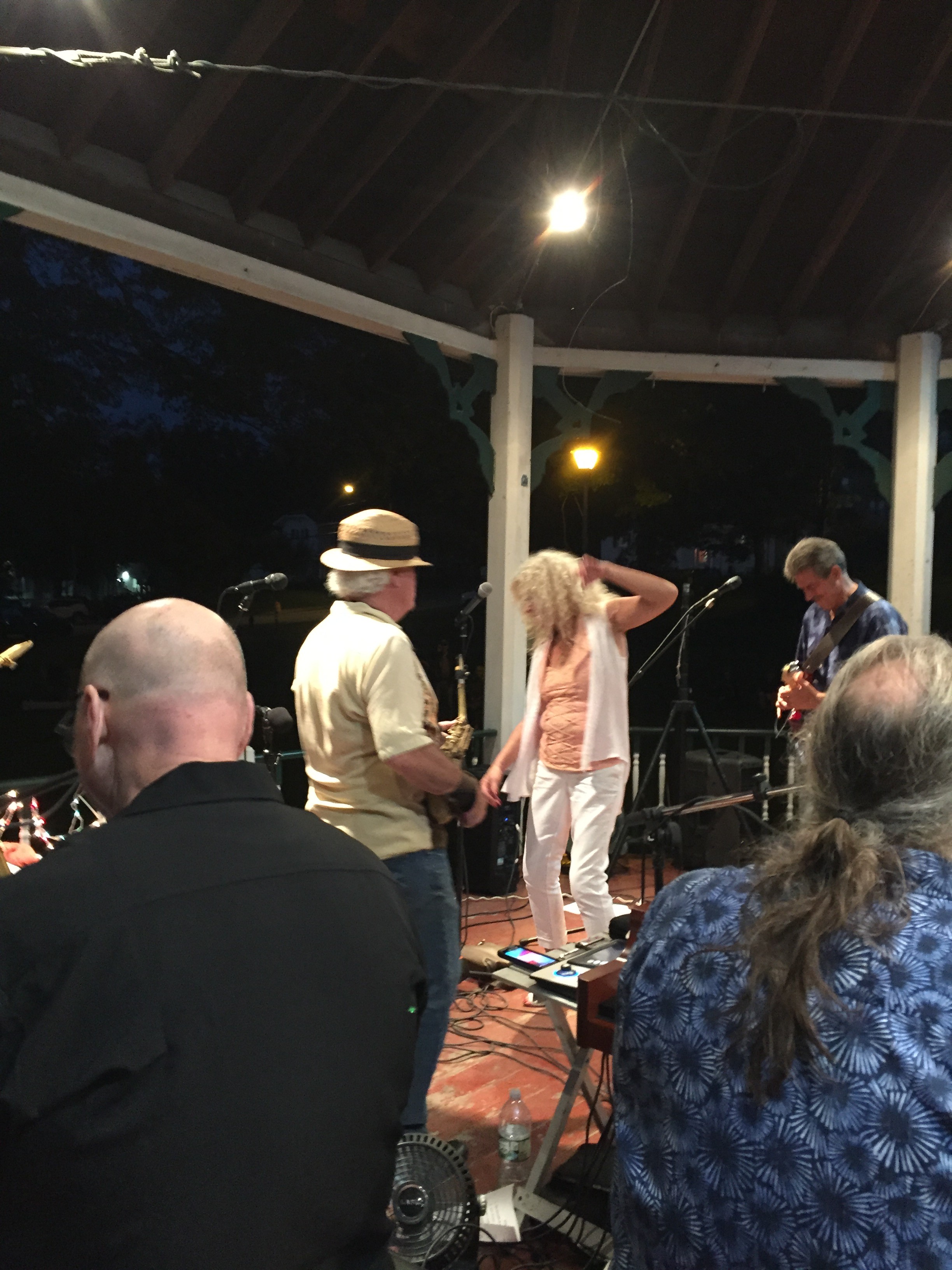 The crowd gathered close to the gazebo as a band plays at dusk.