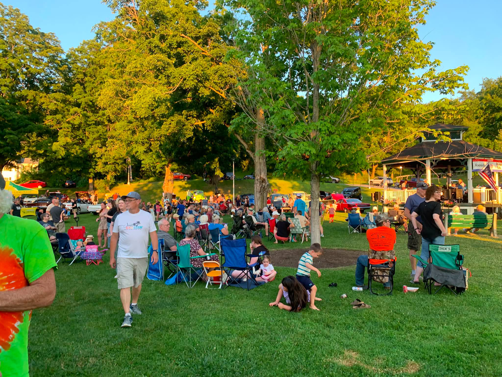 The crowd at golden hour, kids playing on the grass while the music carries across Wood Park.