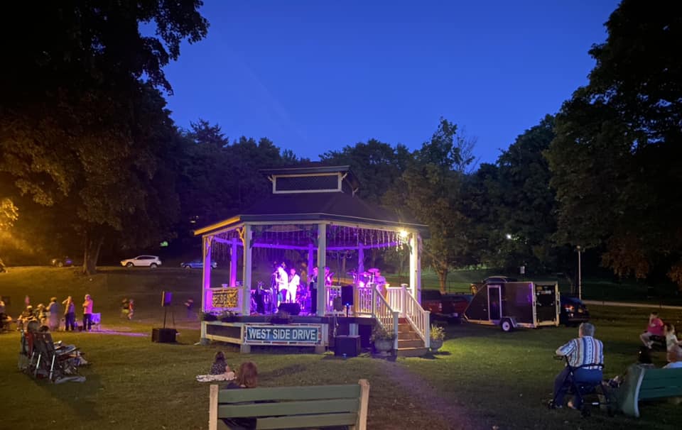 West Side Drive playing the Wood Park gazebo at twilight, neighbors gathered on the lawn.