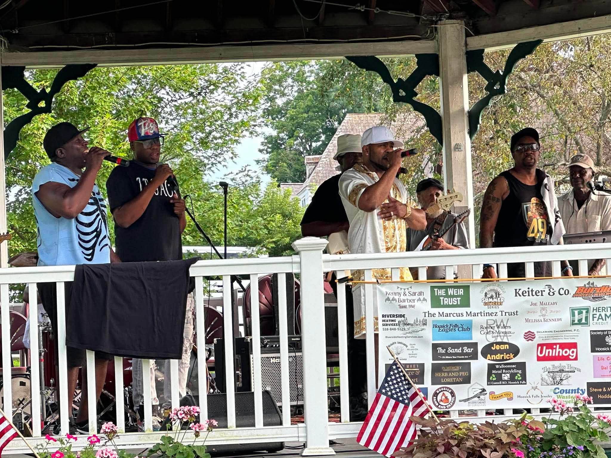 Four Legacy Music Group singers trading verses at the gazebo railing on a summer afternoon.