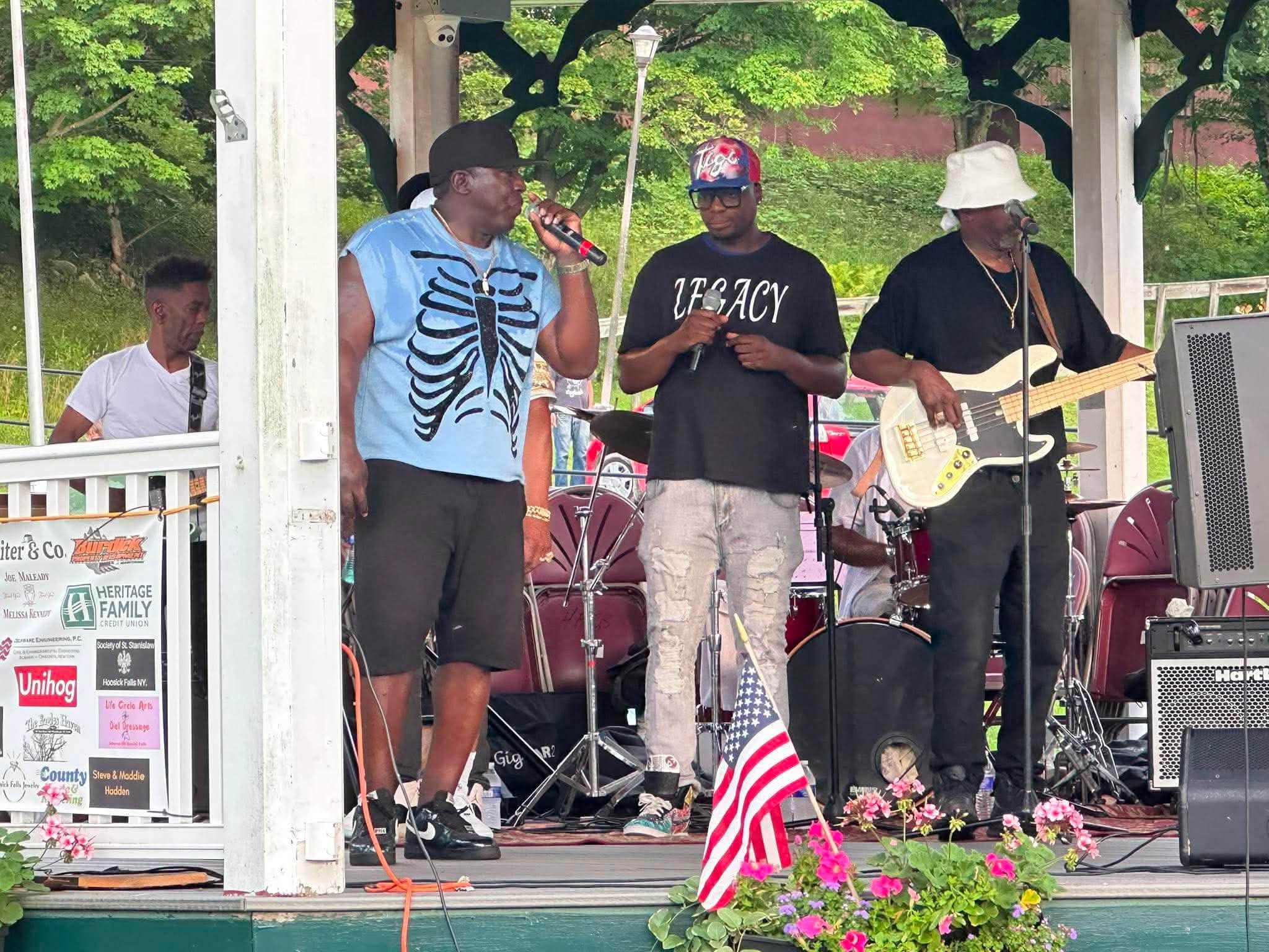 Two Legacy Music Group vocalists sharing a verse at the gazebo mic while the bassist plays behind them.
